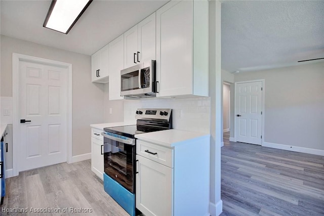 kitchen featuring tasteful backsplash, white cabinets, light wood-type flooring, and appliances with stainless steel finishes