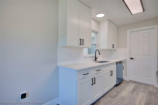 kitchen featuring white cabinetry, sink, stainless steel dishwasher, and light hardwood / wood-style flooring