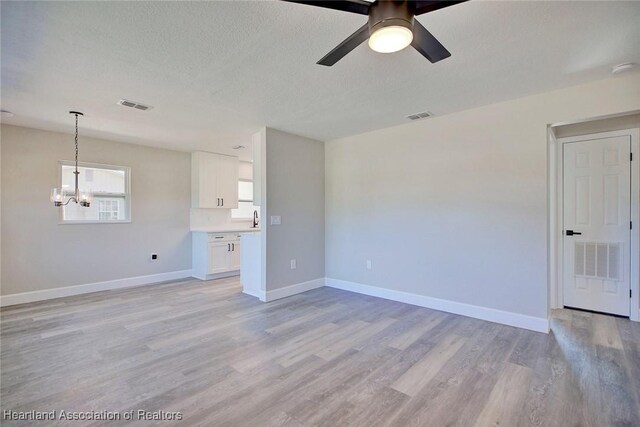 unfurnished living room featuring a textured ceiling, ceiling fan with notable chandelier, and light hardwood / wood-style flooring