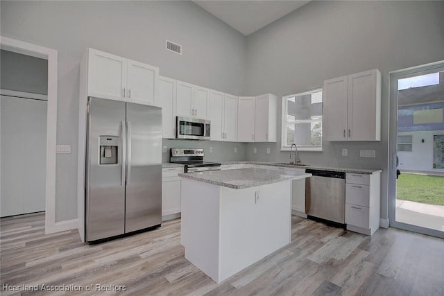 kitchen featuring stainless steel appliances, light hardwood / wood-style flooring, white cabinets, a high ceiling, and a center island