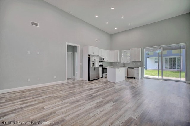 kitchen with a high ceiling, white cabinets, sink, appliances with stainless steel finishes, and a kitchen island