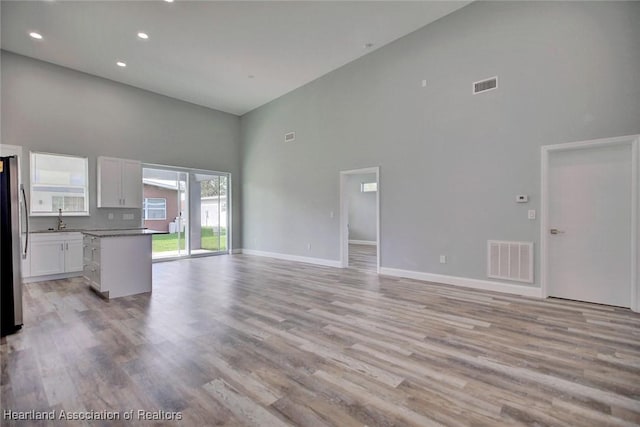 unfurnished living room featuring sink, a towering ceiling, and light wood-type flooring