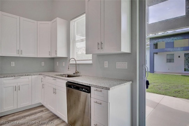 kitchen with light stone countertops, white cabinetry, sink, stainless steel dishwasher, and light wood-type flooring