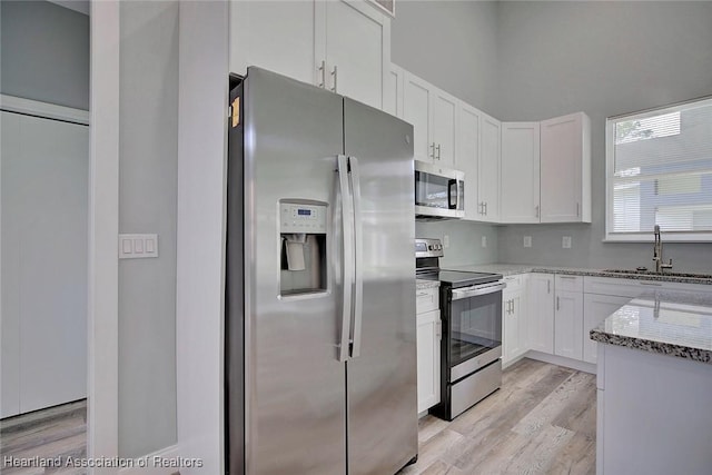 kitchen featuring appliances with stainless steel finishes, light stone counters, sink, light hardwood / wood-style flooring, and white cabinetry