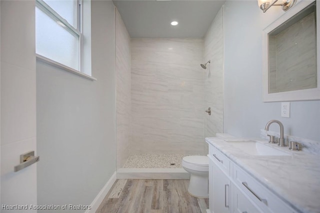 bathroom with toilet, a tile shower, wood-type flooring, and vanity