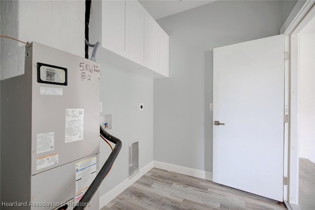 clothes washing area featuring cabinets, electric dryer hookup, heating unit, hookup for a washing machine, and light wood-type flooring