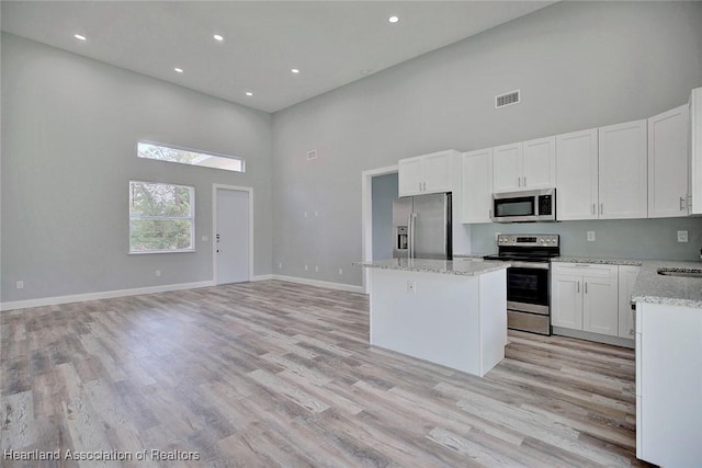 kitchen featuring white cabinetry, a kitchen island, a high ceiling, and appliances with stainless steel finishes