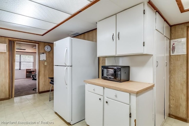 kitchen featuring white refrigerator, white cabinets, and wood walls