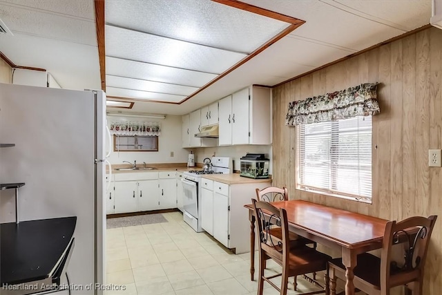 kitchen with white cabinetry, wooden walls, white gas range, and refrigerator