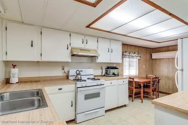 kitchen with white cabinetry, sink, wooden walls, and white appliances