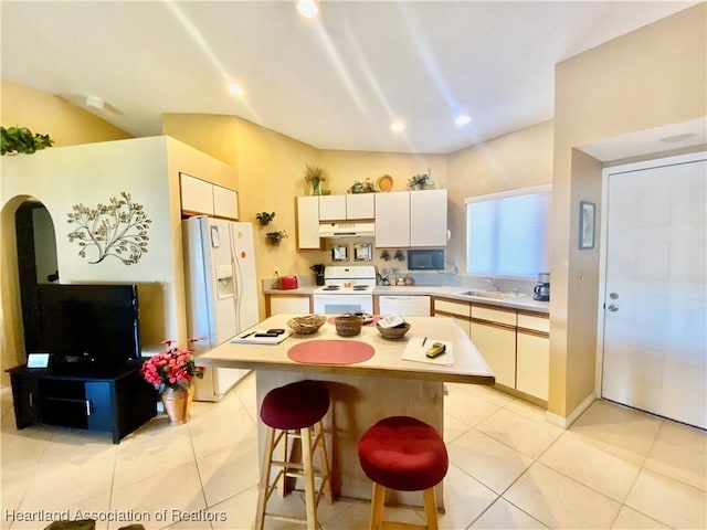 kitchen featuring a breakfast bar, white appliances, sink, a center island, and light tile patterned flooring