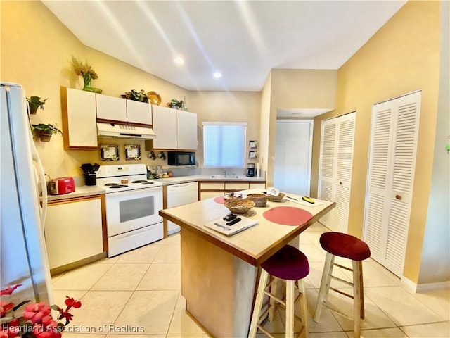 kitchen with white appliances, a kitchen breakfast bar, sink, light tile patterned floors, and a kitchen island