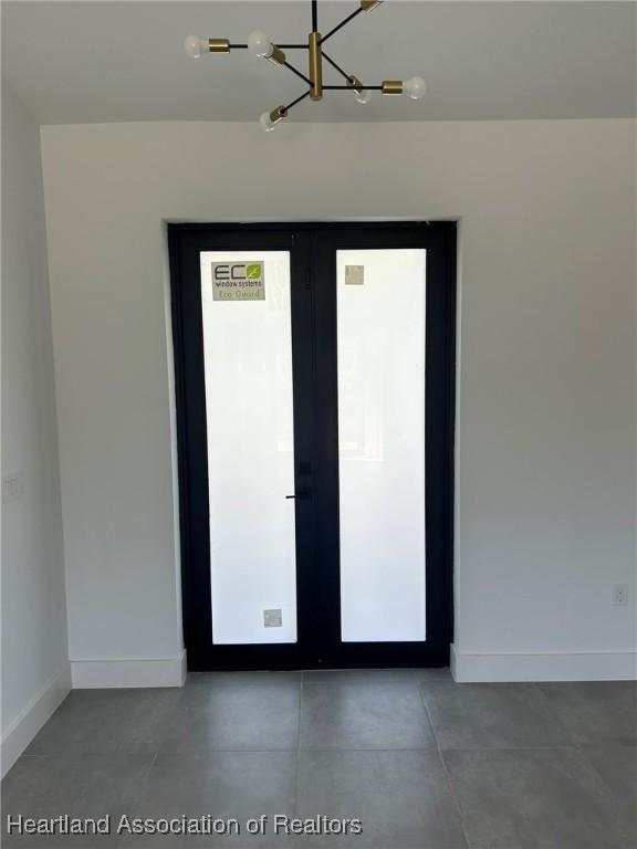 unfurnished room with a notable chandelier, concrete flooring, and french doors