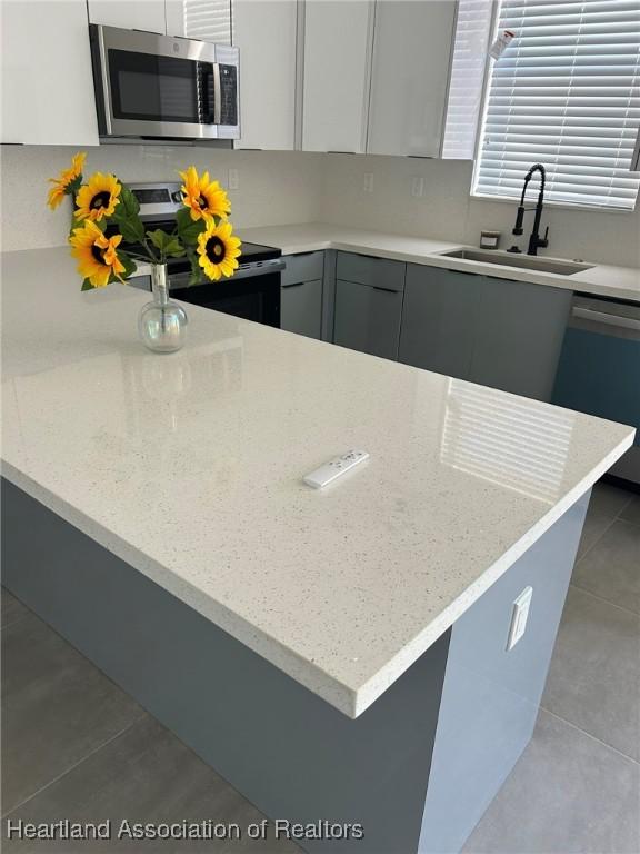 kitchen with sink, gray cabinets, light tile patterned floors, white cabinetry, and stainless steel appliances