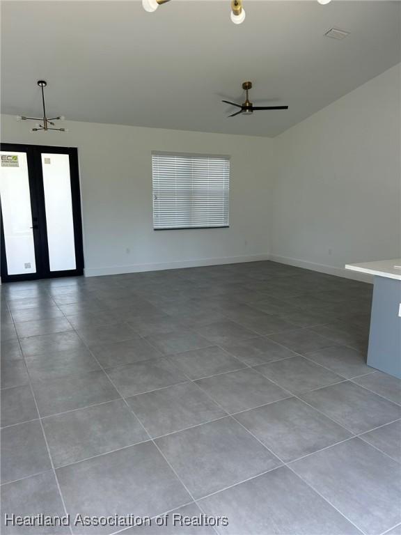 tiled empty room featuring ceiling fan with notable chandelier