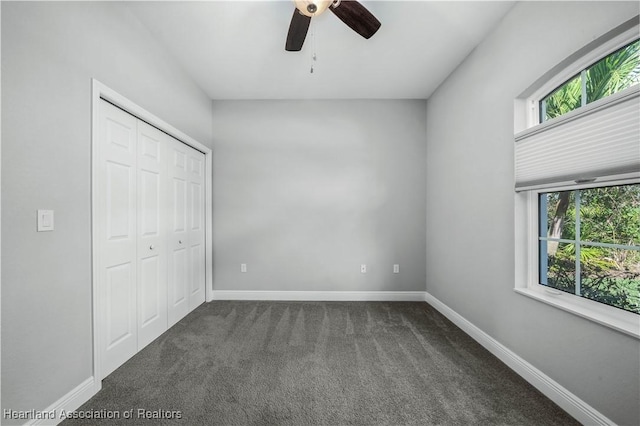 unfurnished bedroom featuring ceiling fan, a closet, multiple windows, and dark colored carpet