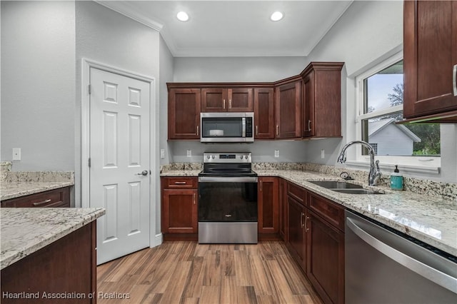 kitchen featuring sink, crown molding, appliances with stainless steel finishes, hardwood / wood-style flooring, and light stone countertops