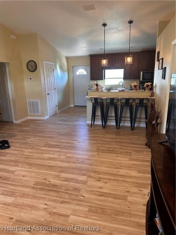 kitchen featuring a breakfast bar, decorative light fixtures, light wood-type flooring, dark brown cabinets, and white fridge