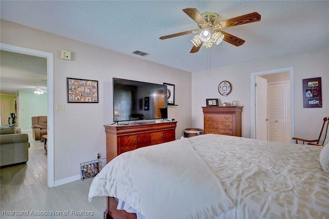 bedroom with a textured ceiling, a ceiling fan, visible vents, wood finished floors, and baseboards