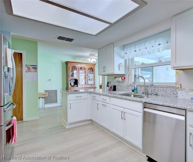 kitchen with white cabinets, a peninsula, a sink, and appliances with stainless steel finishes