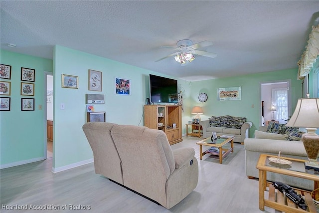 living room featuring ceiling fan, light wood finished floors, baseboards, and a textured ceiling