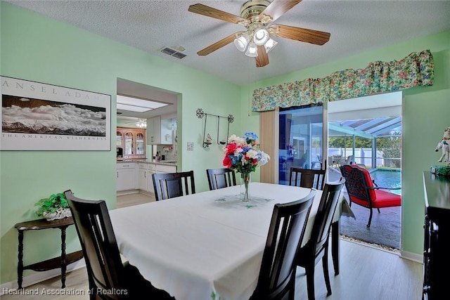 dining room featuring light wood-style flooring, a textured ceiling, visible vents, ceiling fan, and a sunroom