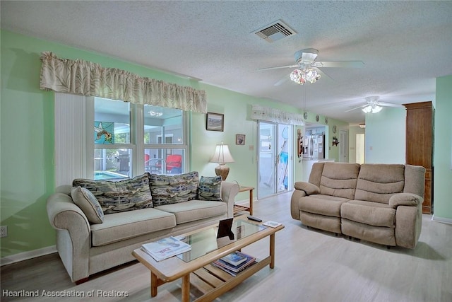 living area featuring a textured ceiling, a ceiling fan, visible vents, wood finished floors, and baseboards