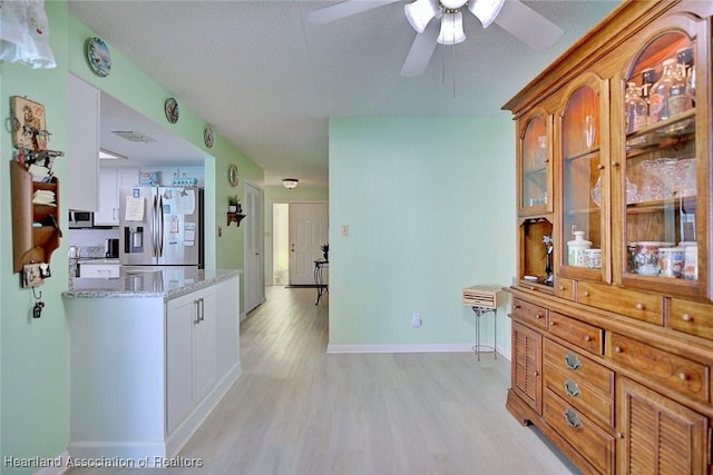 kitchen with baseboards, light wood-type flooring, a ceiling fan, stainless steel refrigerator with ice dispenser, and light stone countertops