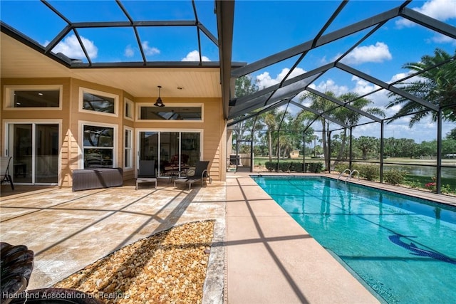 outdoor pool featuring a patio area, a ceiling fan, a water view, and glass enclosure