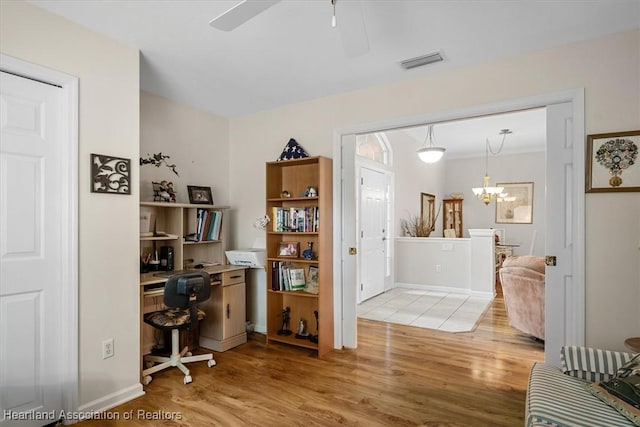 home office featuring ceiling fan with notable chandelier and light hardwood / wood-style flooring