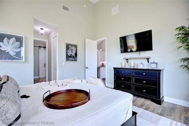 bedroom featuring light hardwood / wood-style flooring, a towering ceiling, and a barn door