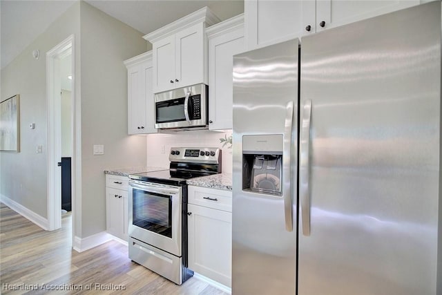 kitchen featuring light stone countertops, appliances with stainless steel finishes, white cabinetry, tasteful backsplash, and light hardwood / wood-style flooring