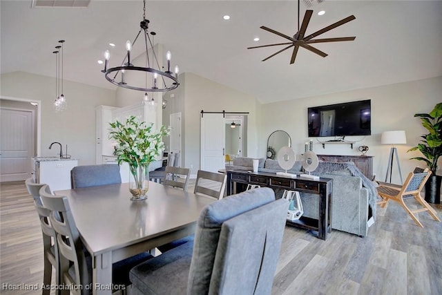 dining space with sink, vaulted ceiling, ceiling fan, light hardwood / wood-style flooring, and a barn door