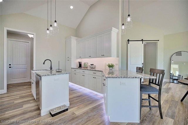 kitchen with white cabinets, decorative light fixtures, light stone counters, a center island with sink, and a barn door