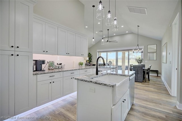 kitchen featuring white cabinets, light stone counters, a kitchen island with sink, and pendant lighting