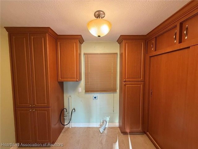 washroom featuring electric dryer hookup, light tile patterned floors, cabinets, and a textured ceiling