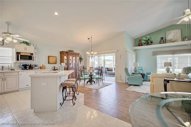 kitchen featuring dishwasher, white cabinets, vaulted ceiling, and a center island with sink