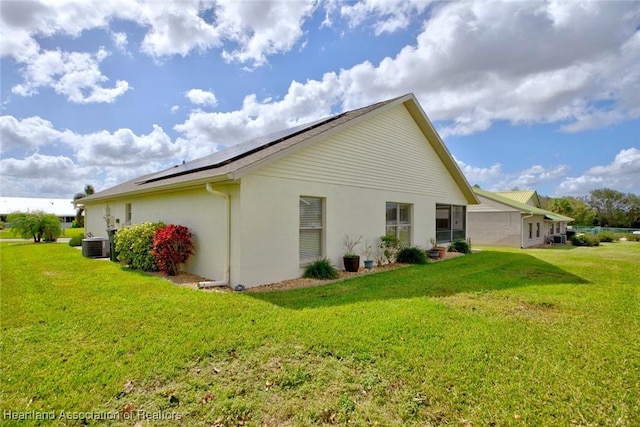 view of home's exterior featuring solar panels, cooling unit, and a lawn