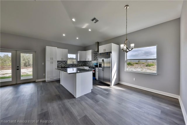 kitchen featuring wall chimney exhaust hood, white cabinetry, a center island, stainless steel fridge, and decorative backsplash