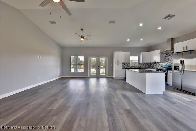 kitchen with wall chimney range hood, appliances with stainless steel finishes, white cabinetry, decorative backsplash, and french doors