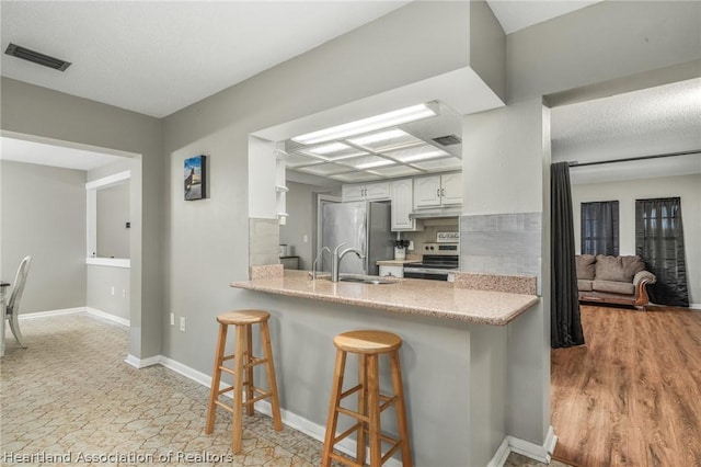 kitchen featuring white cabinets, a kitchen bar, stainless steel appliances, and kitchen peninsula