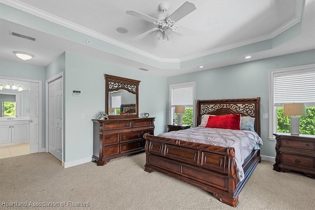 carpeted bedroom with a tray ceiling, ornamental molding, ceiling fan, and ensuite bath