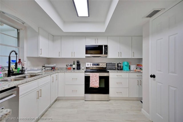 kitchen featuring sink, white cabinetry, stainless steel appliances, and a tray ceiling