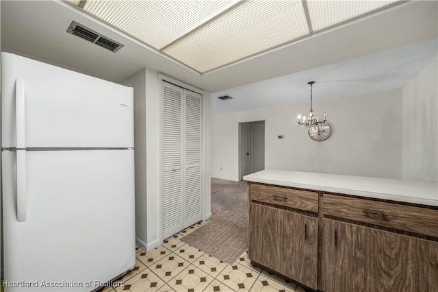 kitchen with white refrigerator, dark brown cabinetry, a chandelier, and decorative light fixtures