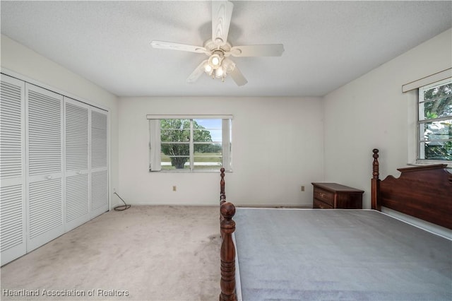 carpeted bedroom with a textured ceiling, ceiling fan, and a closet