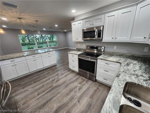 kitchen with light stone countertops, appliances with stainless steel finishes, decorative light fixtures, hardwood / wood-style flooring, and white cabinets