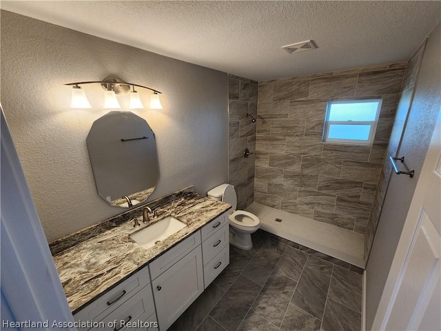 bathroom with vanity, toilet, a textured ceiling, and a tile shower