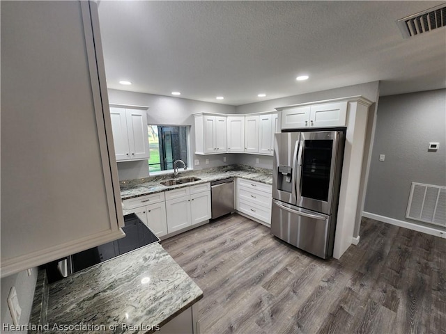 kitchen with light stone countertops, stainless steel appliances, white cabinetry, and sink