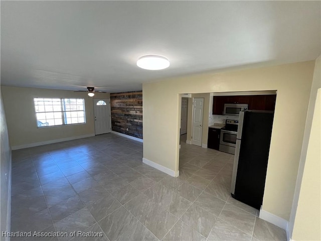 unfurnished living room featuring ceiling fan and wooden walls