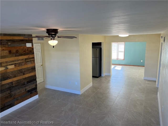 empty room featuring ceiling fan and wooden walls